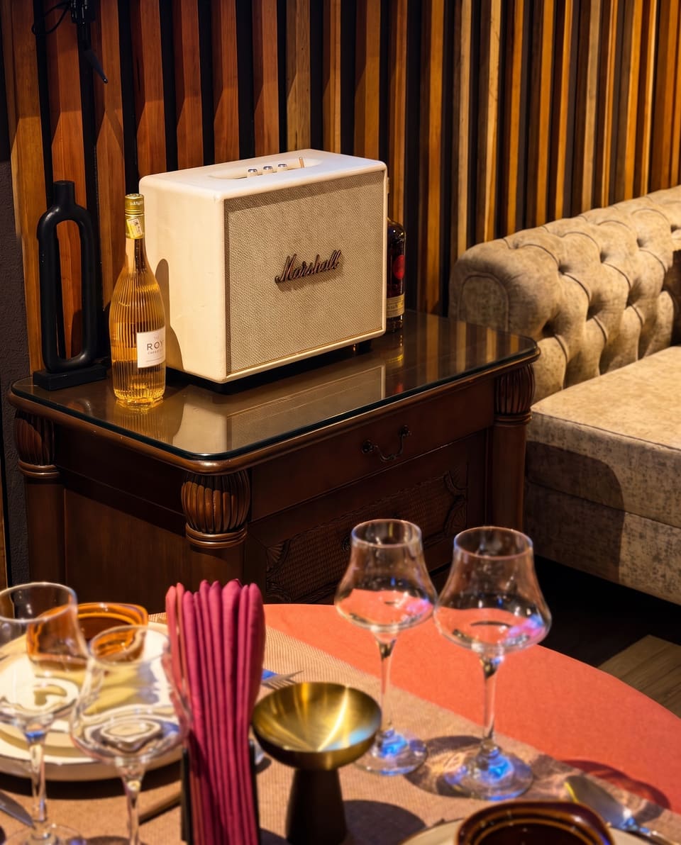 Canto do lounge com coluna Marshall, garrafa de rosé e sofá chesterfield